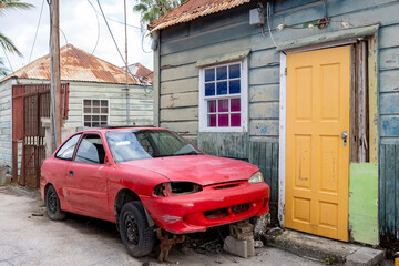 Side street with small weathered house and a broken red car in the front in the suburbs of Willemstad, Curacao