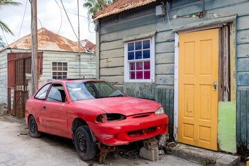 Side street with small weathered house and a broken red car in the front in the suburbs of...
