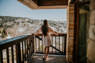 Charming young woman in bathrobe enjoying the winter nature on the large terrace