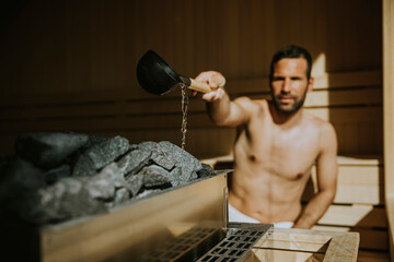 Young man pouring water onto hot stone in the sauna