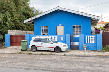 White compact car on the sidewalk in front of a blue painted house in the suburbs of Willemstad,...