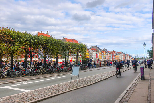 Bicyclists ride past parked bicycles along the Nyhavn Canal in the historic, touristic district of Copenhagen Denmark.
