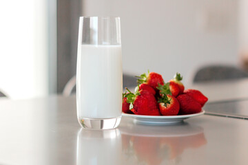 Glass of milk and plate with pile of fresh strawberries set on the table.