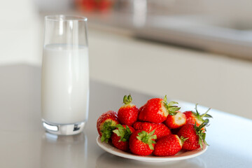 Glass of milk and plate with pile of fresh strawberries set on the table.