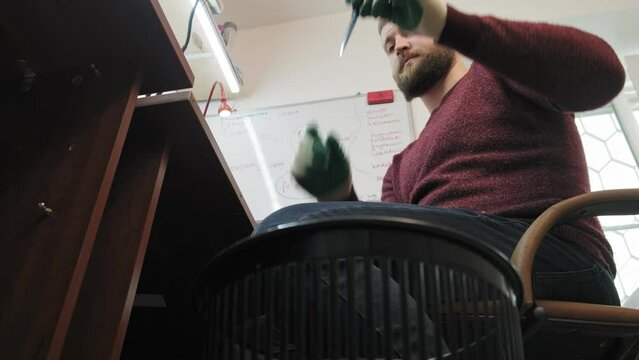 A uniformed worker in the garage of a mechanical workshop checks his tool and throws the unusable one into the trash