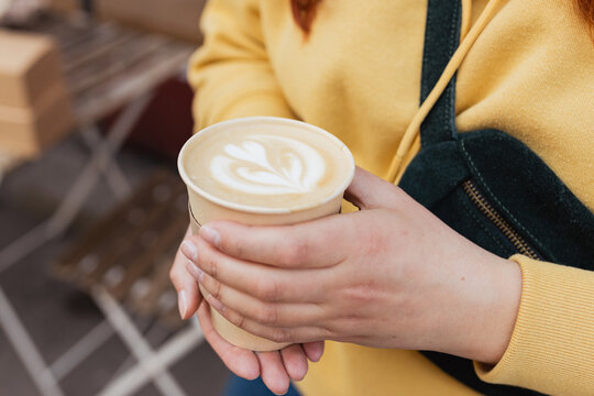 Bio paper cup with coffee latte art in woman hand. Young stylish hipster redhead girl drinking hot latte. Traveler. Take away delivery concept. Eco recycle environment friendly.