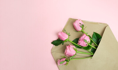 Pink roses in a craft paper envelope on a pink background. Greeting card for birthday, Mother's Day, Valentine's Day. Romantic message concept. Top view, flat lay, copy space.