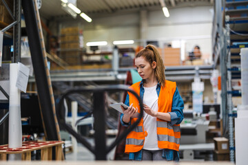 Woman with tablet in factory storehouse checking location of goods