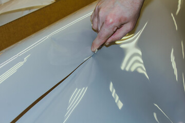 A man cuts off a polyurethane film with a knife.  The process of cutting off the desired piece of...