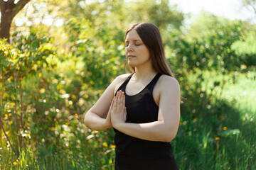 The brunette folded her hands in a namaste gesture during a yoga class in a city park. Summer, green grass, healthy lifestyle during the coronavirus pandemic