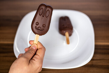 A hand holding a filled chocolate cake pop or cakesicle in a popsicle shape