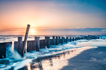 Seascape of wooden breakwater pier at sunrise with ocean tide - obrazy, fototapety, plakaty