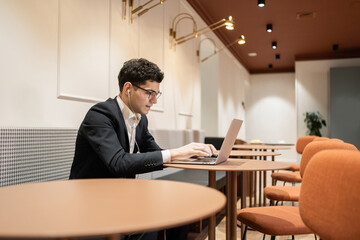 A business man with glasses in a suit uses a laptop computer works in an office coworking space