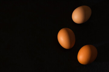 Natural home product. Fresh brown eggs with hard shadows on a dark background. Minimalism. Top view. Copy space.