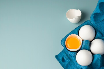 Farm natural products. Chicken fresh eggs in eco-packaging on a blue background. Broken egg with...