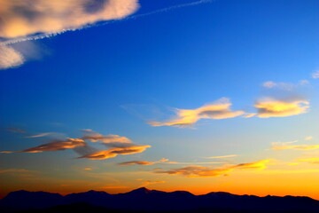 Yellow-blue sunset sky with the clouds shaped in a bizarre figure over the silhouettes of the...