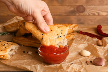 Woman dipping tasty Uzbek samsa into tomato sauce in bowl on table