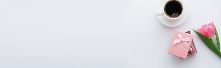 top view of cup of coffee near pink tulip and gift box on white, banner.