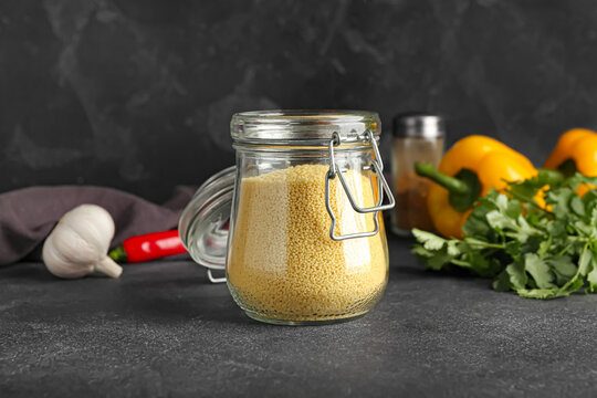 Jar with raw couscous on dark background