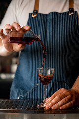 man bartender hand holds a small bottle and pours an alcoholic drink from it into a glass
