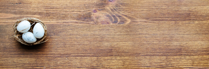 three white eggs in a nest on a wooden background. Banner, extra-wide format, copy space