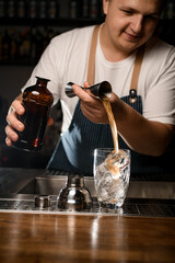 Male bartender pours liquid from jigger into crystal mixing cup