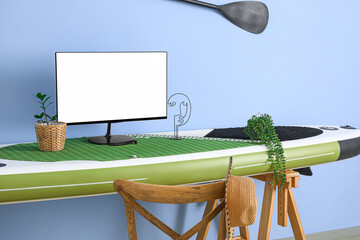 Modern computer on table made of sup surfing board near color wall