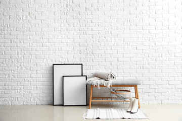 Soft bench with plaid, basket, shoes and blank frames near white brick wall