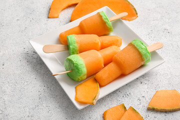 Plate with tasty melon popsicles on light background