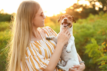 Young woman holding cute Jack Russel dog in park - obrazy, fototapety, plakaty