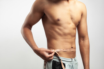 Caucasian young man measuring his abdomen belly size by a tape measure isolated in white background.