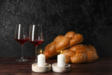 Glowing candles with traditional challah bread and wine on dark background. Shabbat Shalom