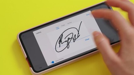 Electonic signature with finger in phone screen on yellow background desk.