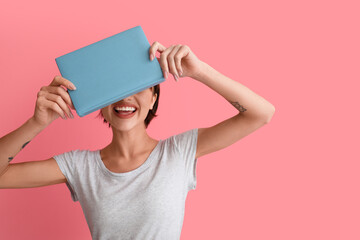 Beautiful young woman with book on pink background