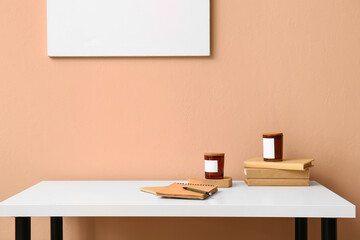 Notebooks, books and candles on table near color wall