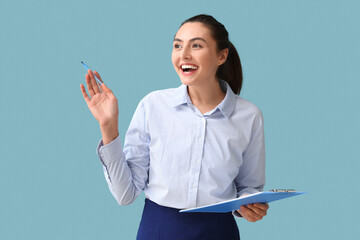 Pretty young businesswoman with clipboard on blue background