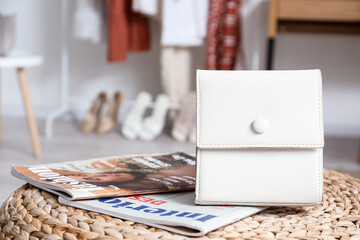 Stylish bag and fashion magazines on pouf in room