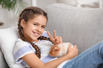 Little girl with cute guinea pig on sofa