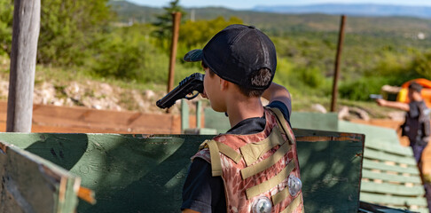 Fototapeta premium boy from the back in a military suit with a toy gun pointing at the horizon