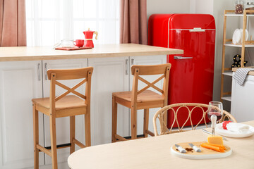 Interior of light kitchen with retro fridge, white counters and chairs