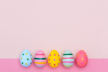Fototapeta na wymiar Easter border of bright Easter eggs on two-tones pink background. Multi-colored striped and dotted eggs in a row with copy space.