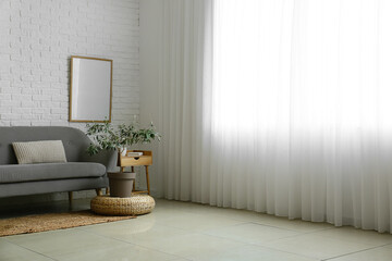 Sofa, houseplant and blank photo frame in light room interior