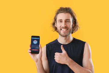 Sporty man holding phone with installed app for calories counting and showing thumb-up on color background