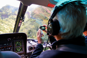Old man filming with an action camera on the front row of a helicopter in a lush valley on Kauai...