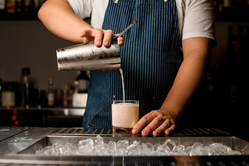 bartender pours cocktail from shaker into glass standing on metal bar counter