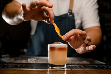 Bartender adding orange zest to a brown cocktail in the glass