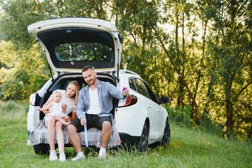 Family with kid sitting in car trunk - obrazy, fototapety, plakaty