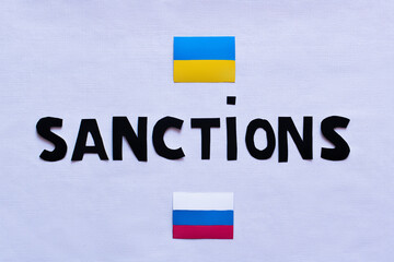 Fototapeta na wymiar Top view of sanctions lettering near ukrainian and russian flags on white background.