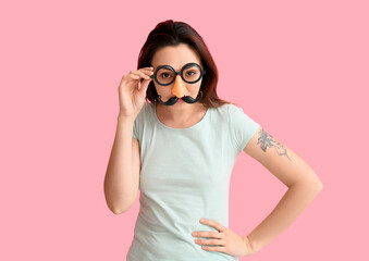 Young woman in funny disguise on pink background. April fools' day celebration