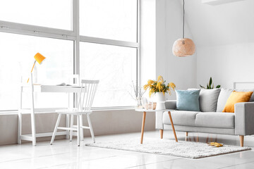 Vase with mimosa flowers on table and sofa in interior of living room